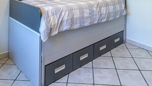 Ein Einzelbett mit Stauraumschubladen, eine Hängeleuchte und schlichte Wände.