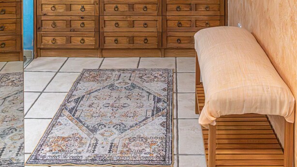 Ein Zimmer mit einer hölzernen Sitzbank, einem gemusterten Teppich und einer Wand mit Holzkästchen.
