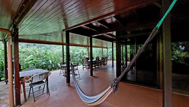 A covered outdoor area with tables and chairs, a hammock, and a view of lush greenery. - An unrivalled Location: Situated in the heart of Costa Rica's adventure capital, (Alajuela)
