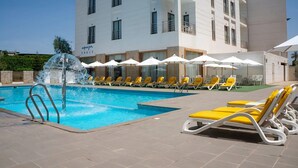 A swimming pool with a water fountain, yellow lounge chairs, and umbrellas. - Hotel Le Zenith Oran (Es Senia)