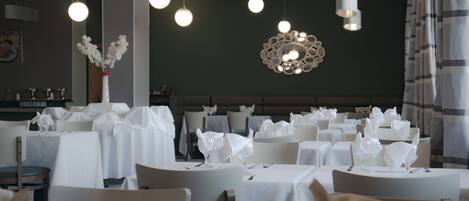 Un restaurante con mesas redondas cubiertas con manteles blancos, cada una con servilletas y cubiertos blancos.