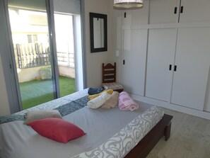 A bedroom with a bed, a bench, a wardrobe, and a view of a garden through a sliding door.