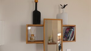 A wall-mounted shelf with a black bottle, a white vase with dried plants, and a mirror reflecting a room with a piano.