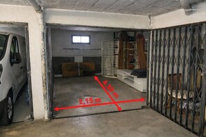 A garage with a car parked on the left, a window above a door, and a metal gate on the right.