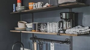 Une cuisine équipée d’une cuisinière intégrée, d’un évier et d’une étagère au-dessus du plan de travail, où sont rangés divers ustensiles de cuisine.