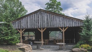 Un bâtiment rustique en bois, doté d’un patio couvert, de sièges en pierre et entouré d’un cadre naturel.