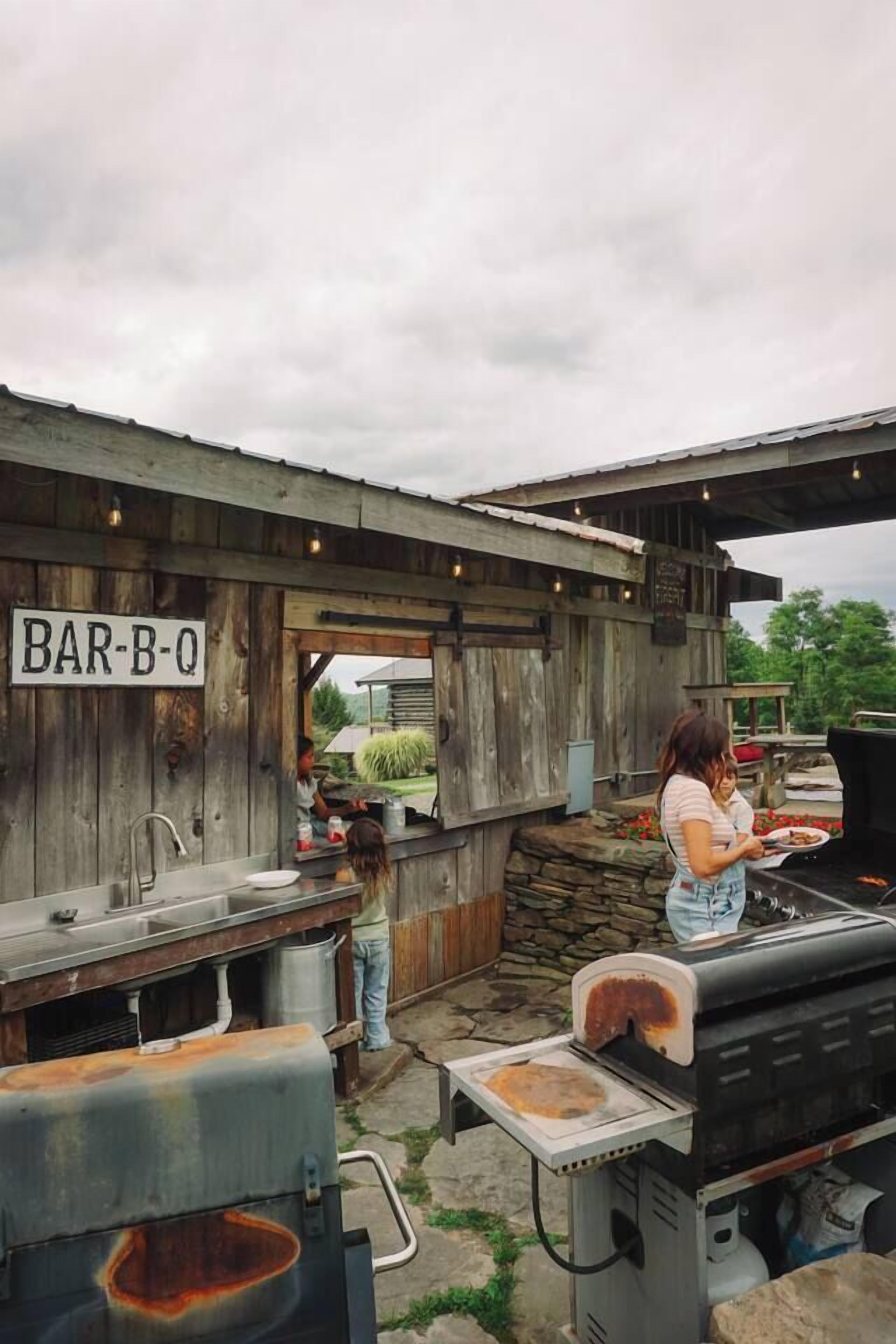 Ein Außenbereich mit Bar, gestaltet als rustikale Holzkonstruktion, inklusive Grill und einem Schild mit der Aufschrift 'BAR-B-Q'.