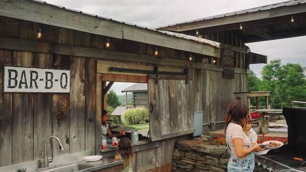 Un área de bar al aire libre con estructura de madera rústica, una parrilla y un letrero que dice 'BAR-B-Q'.
