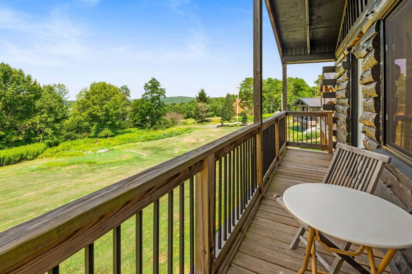 A wooden deck with a table and chairs, overlooking a well-maintained lawn and trees.