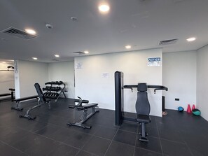 Une salle de sport équipée de divers appareils d’entraînement, notamment des haltères, un banc de développé couché et un support à squats.