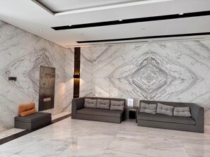 Un hall d’entrée moderne avec des murs en marbre, un enrouleur de tuyau d’incendie, une vanne d’arrêt et deux canapés gris.