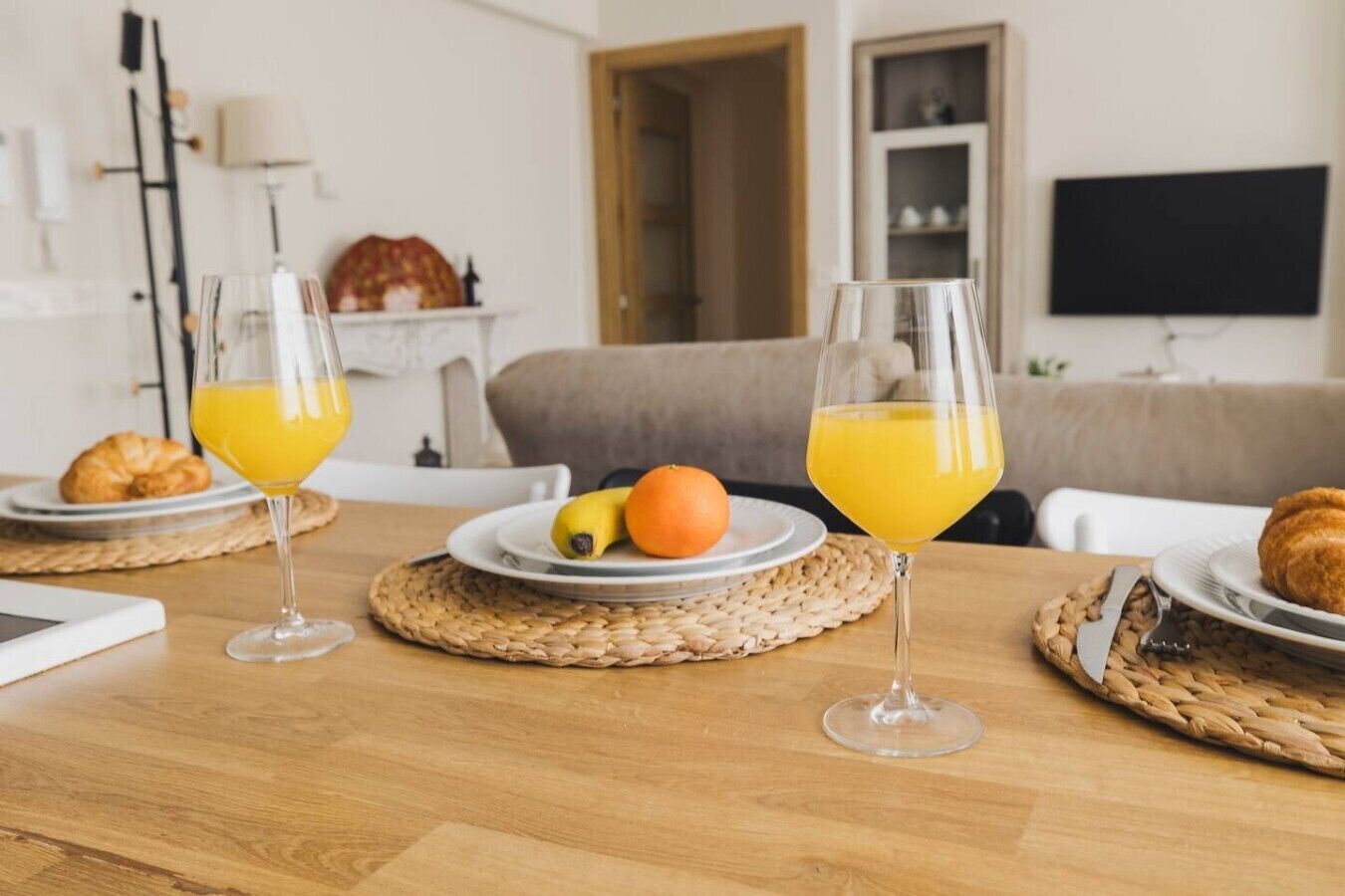 Une table en bois dressée pour le petit-déjeuner, avec deux assiettes de fruits et des verres de jus.
