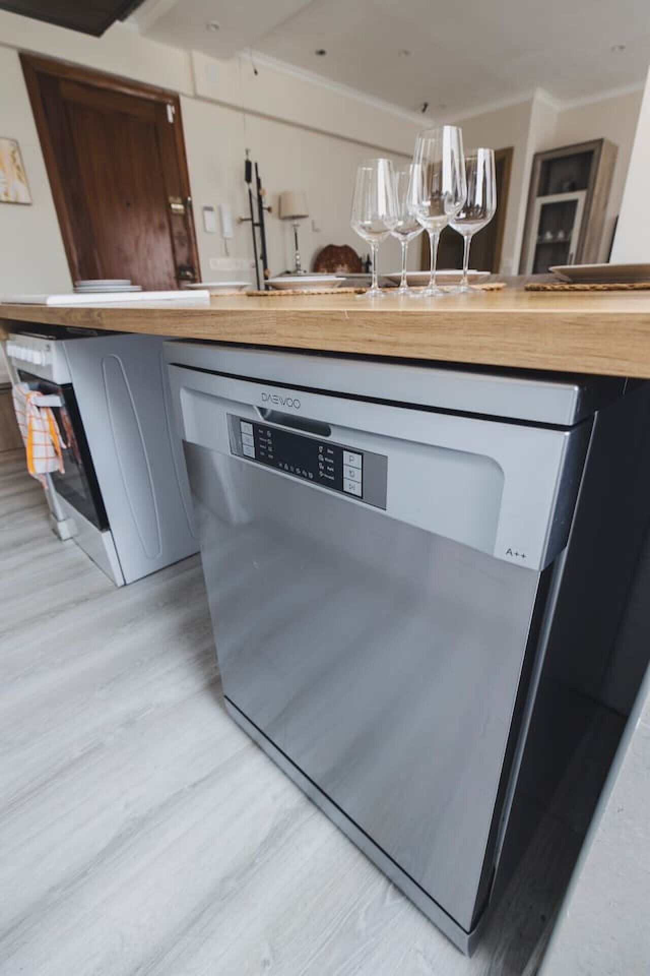 Una cucina moderna con lavastoviglie integrata, un piano di lavoro in legno e un set di bicchieri da vino sopra.