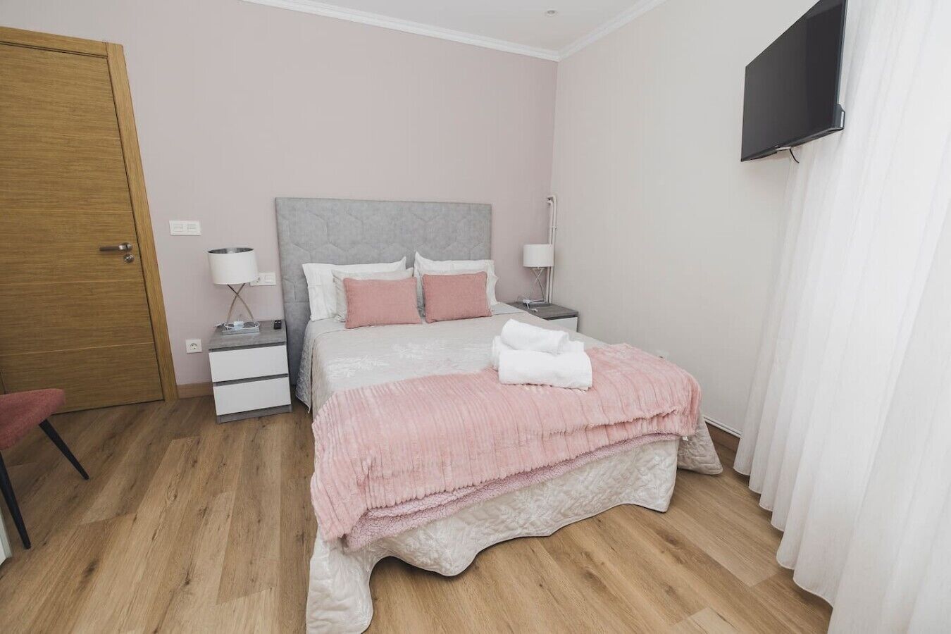 Una camera da letto ordinata con un letto, comodini, una TV e una porta.