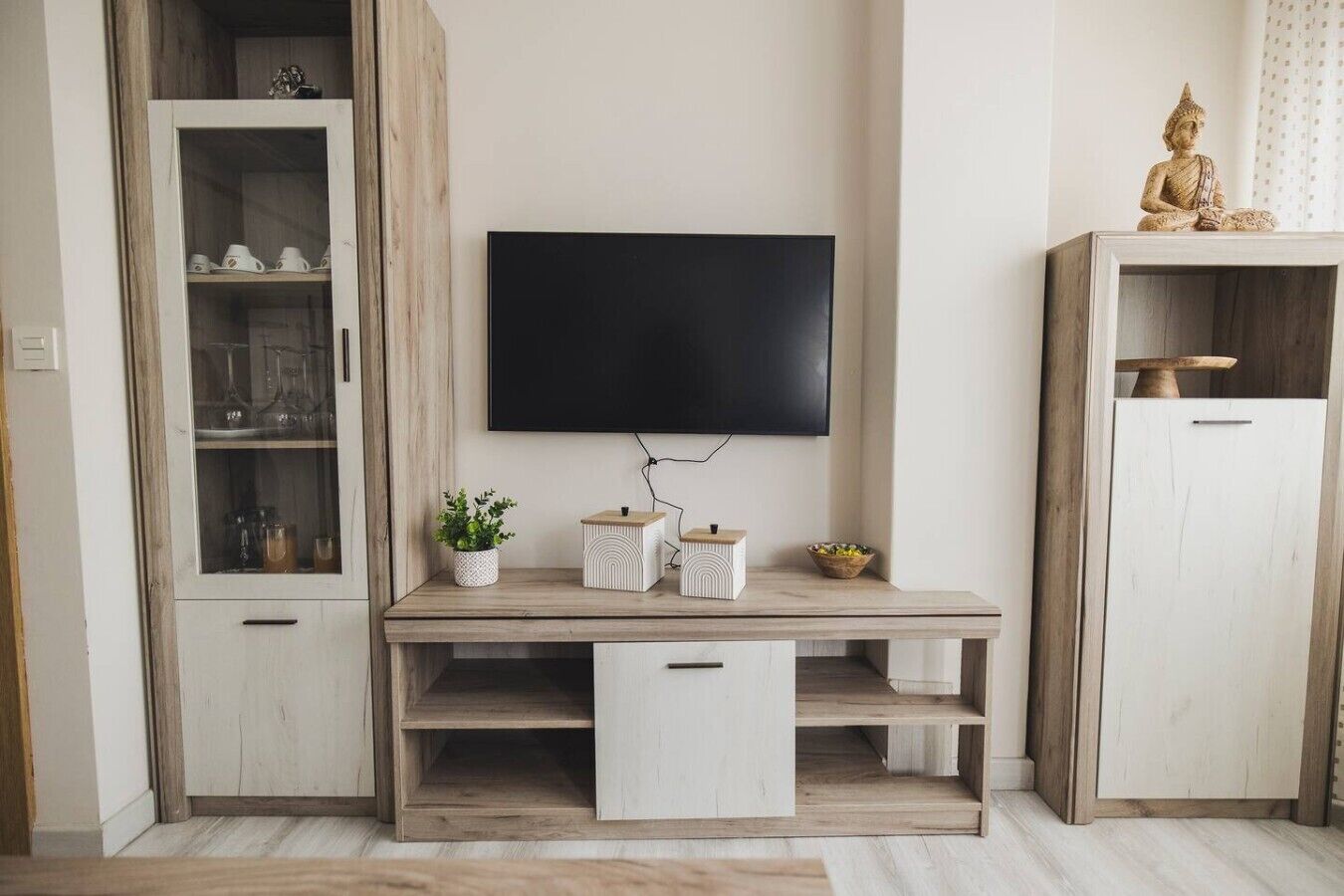 Una sala de estar moderna con un televisor de pantalla plana montado en la pared, muebles de madera y objetos decorativos.