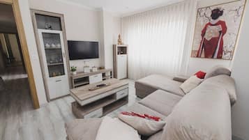 Een moderne woonkamer met een zithoek, een flatscreen-tv, een houten salontafel en een decoratieve Boeddha-beeldje.