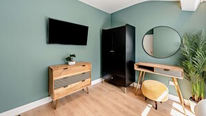 Een moderne slaapkamer met een flatscreen televisie, een zwarte garderobe, een houten bureau en een ronde spiegel.