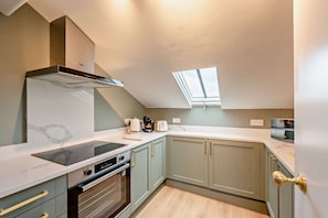 A compact kitchen with a built-in oven, a stovetop, and a microwave. There is a skylight above the counter, and the cabinets are light green with gold handles. - Host Stay The Georgian Quarter Catharine V (Liverpool)