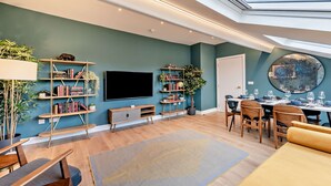 Een moderne woonkamer met een flatscreen televisie, boekenkasten, een eethoek met stoelen en een tafel voor vier personen, en een dakraam erboven.