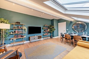 A modern living room with a flat-screen TV, bookshelves, a dining area with chairs and a table set for four, and a skylight above. - Host Stay The Georgian Quarter Catharine V (Liverpool)