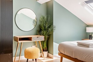 Ein Schlafzimmer mit Bett, Nachttisch, Lampe, Spiegel, Schreibtisch, Stuhl und einer Topfpflanze.