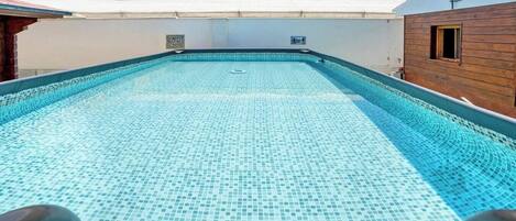 Una piscina en la azotea con suelo de baldosas y un cielo azul despejado.