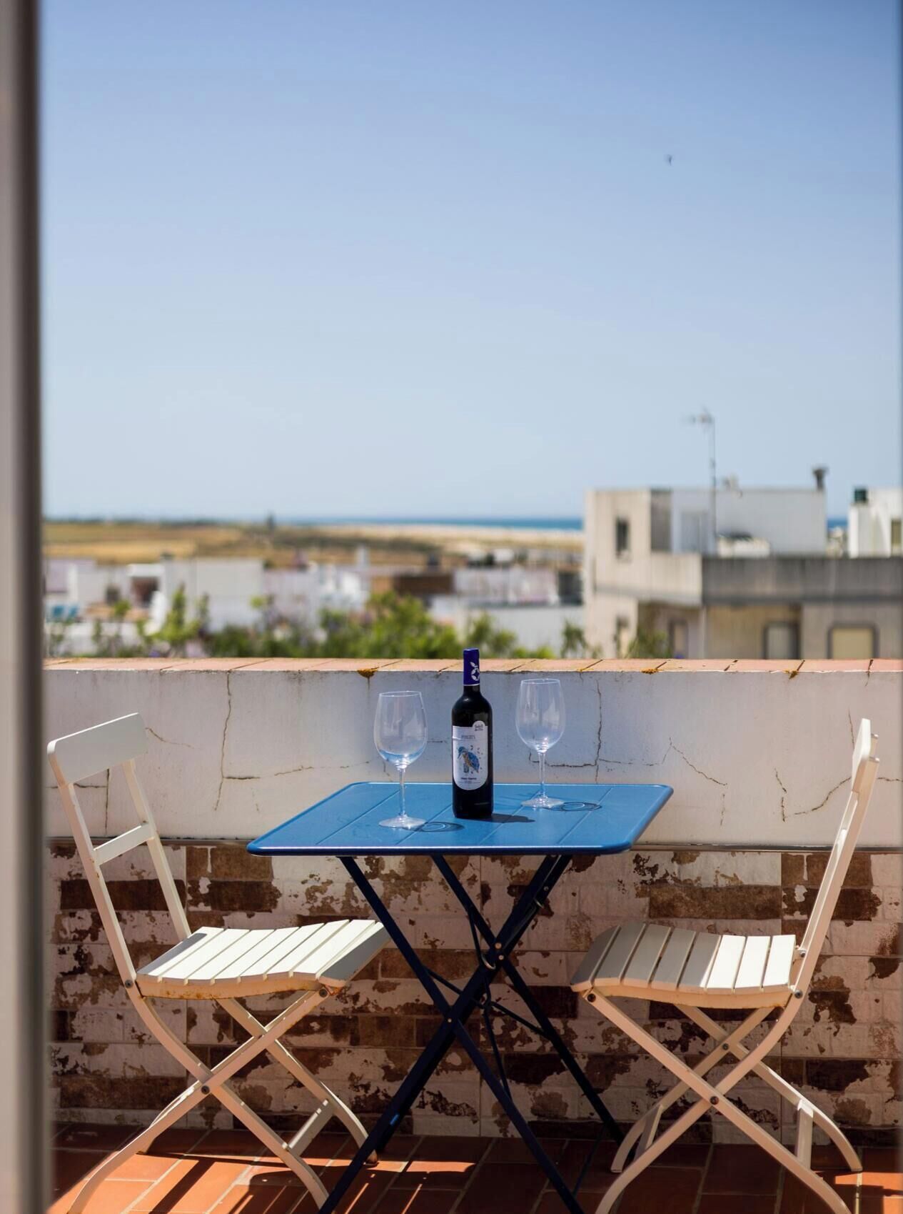 Un balcon avec une table, deux chaises, une bouteille de vin et deux verres.