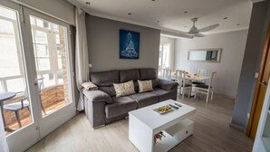 Ein modernes Wohnzimmer mit grauem Sofa, weißem Couchtisch und einem Essbereich mit weißem Tisch und Stühlen.