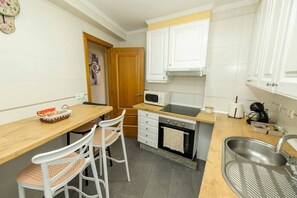 A compact kitchen with white cabinets, a microwave, a sink, and a dining area with two chairs. - Central Bright Apartment · Beach & Rías Baixas (Vilagarcía de Arousa)