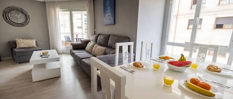 A modern living room with a grey sofa, a white coffee table, and a dining area with breakfast items.