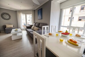 A modern living room with a grey sofa, a white coffee table, and a dining area with breakfast items. - Central Bright Apartment · Beach & Rías Baixas (Vilagarcía de Arousa)