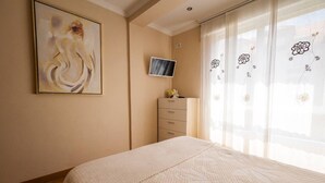 Ein Schlafzimmer mit einem Bett, einem Fernseher an der Wand, einer Kommode und einem Gemälde.