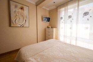 Un dormitorio con cama, televisor en la pared, cómoda y un cuadro.