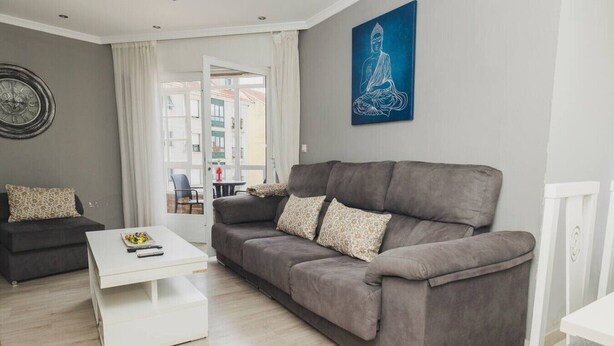 Ein modernes Wohnzimmer mit grauem Sofa, einem weißen Couchtisch und einem blauen Kunstwerk an der Wand.