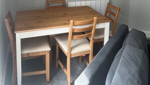 Ruokailutila, jossa on puinen pöytä ja tuolit, seinälle kiinnitetty kello ja patteri.