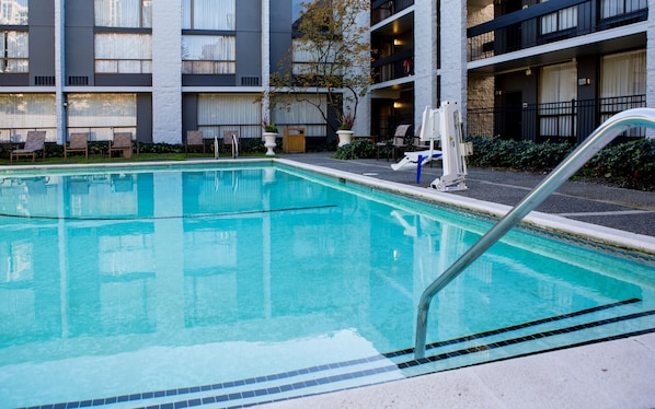 Ein Swimmingpool mit Metallleiter, umgeben von einem Gebäude mit mehreren Balkonen und Fenstern.