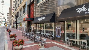 An outdoor seating area with tables and chairs, a storefront with signage, and a pedestrian walkway.