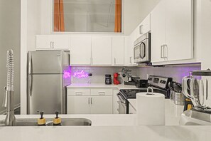 A modern kitchen with white cabinets, stainless steel appliances, a built-in microwave, and a neon sign.