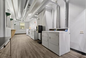 A laundry facility with multiple washing machines, a drying machine, and a control panel. - New Downtown Indy Group Stay +4BR+Sleeps 14 (Indianapolis)