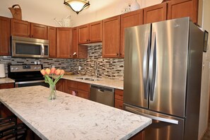 A kitchen with wooden cabinets, a stainless steel refrigerator, a microwave, and a sink. - 2 min walk to gondola! (Vail)