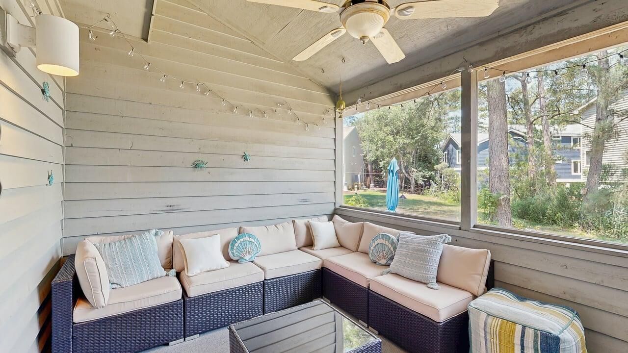 A covered porch with a wicker sofa, ceiling fan, and string lights.