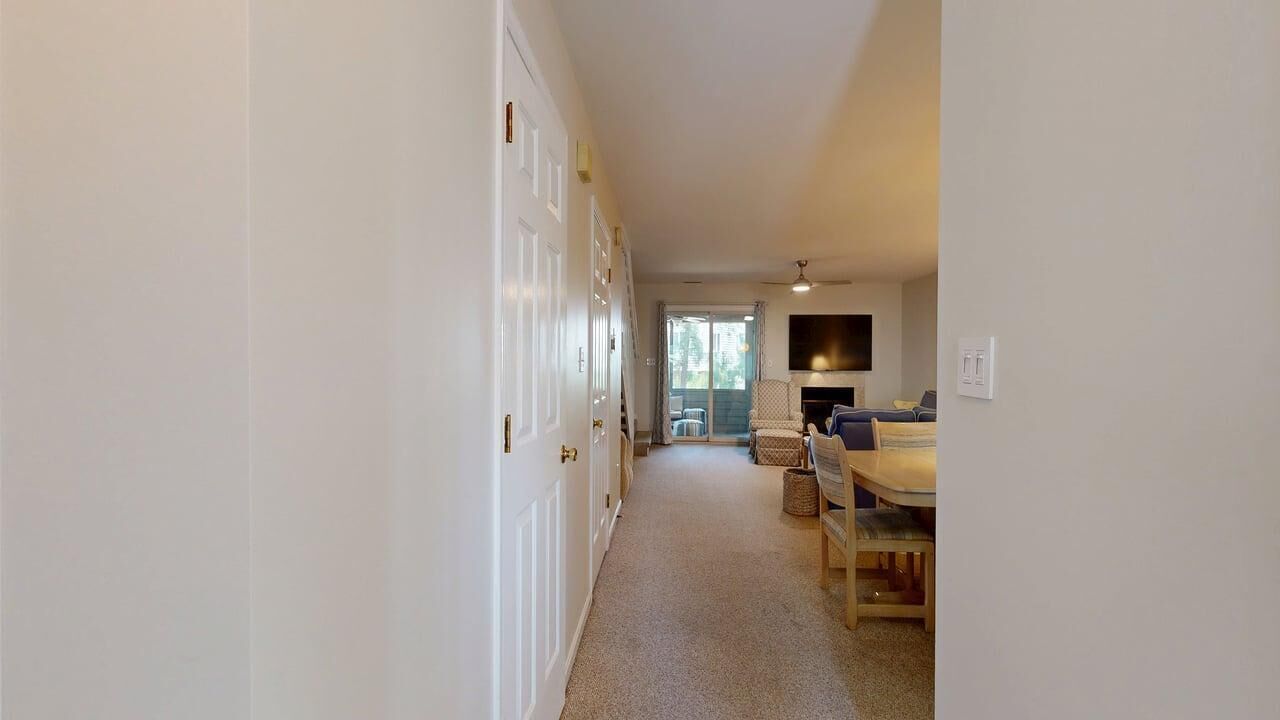 A hallway leading to a dining area with a table and chairs, a sofa, and a television.