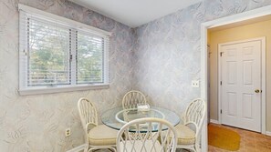 A dining area with a glass table and white chairs, a window with blinds, and a door with a doormat. - Bethany Beach - 830 Westwood Ave Unit C (Bethany Beach)