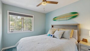 Ein Schlafzimmer mit einem Bett, einem Deckenventilator, einem Fenster und einer Surfbrettdarstellung.
