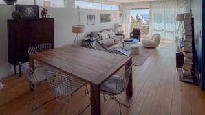 A modern living room with a wooden dining table, two chairs, a sofa, and a balcony with a view. - Beautiful apartment just a stone's throw from Paris, in a quiet neighborhood (Saint-Cloud)