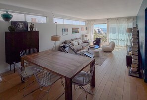 Ein modernes Wohnzimmer mit Esstisch aus Holz, zwei Stühlen, einer Couch und einem Balkon mit Blick.