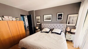 A bedroom with a large bed, a wardrobe, a bedside table with a lamp, and a bookshelf. - Beautiful apartment just a stone's throw from Paris, in a quiet neighborhood (Saint-Cloud)