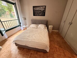 Ein Schlafzimmer mit Bett, Nachttisch, Lampe, Kleiderschrank und einem Stadtbild an der Wand.