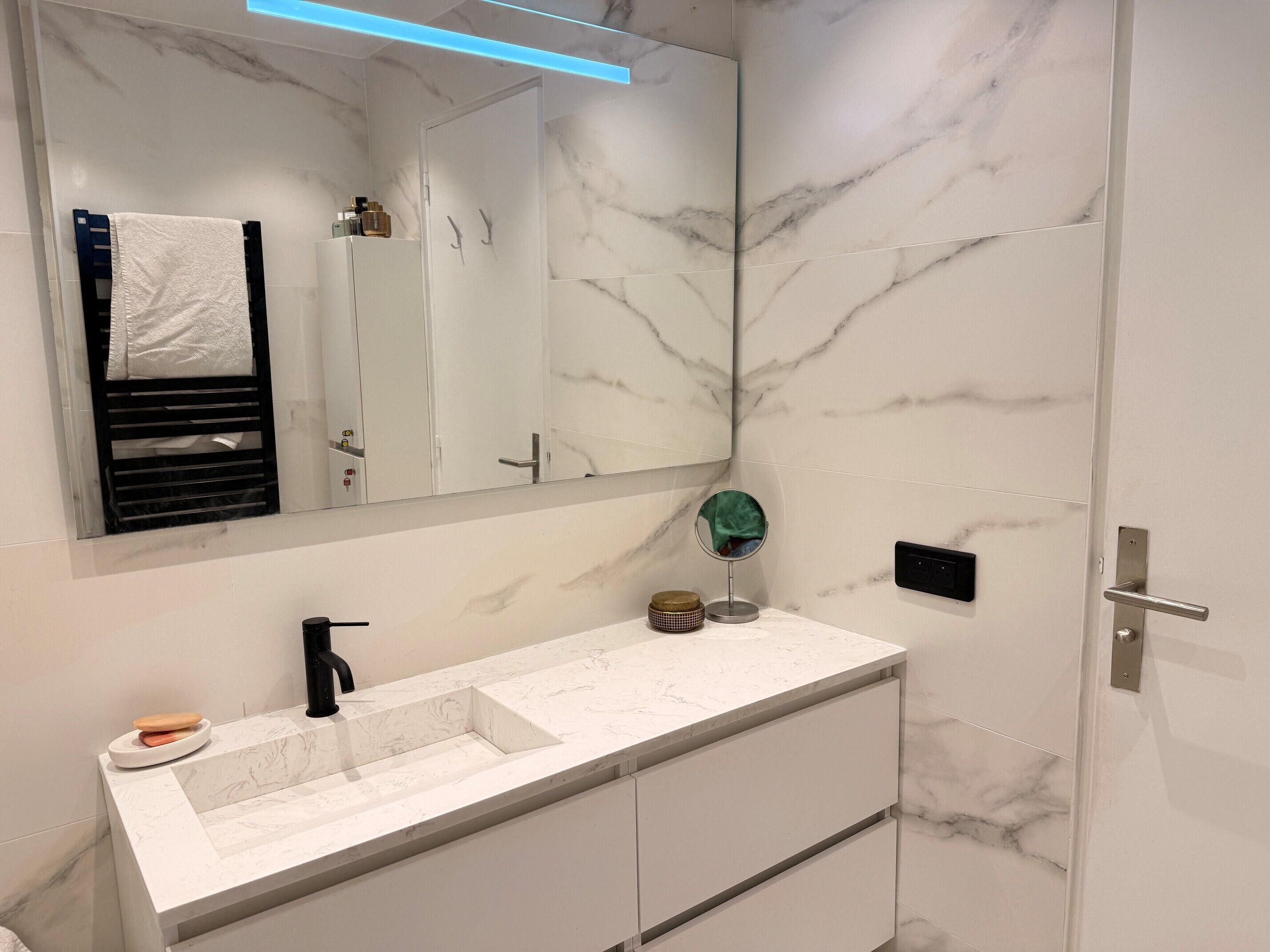 A bathroom with a white marble sink, a mirror, and a towel rack.
