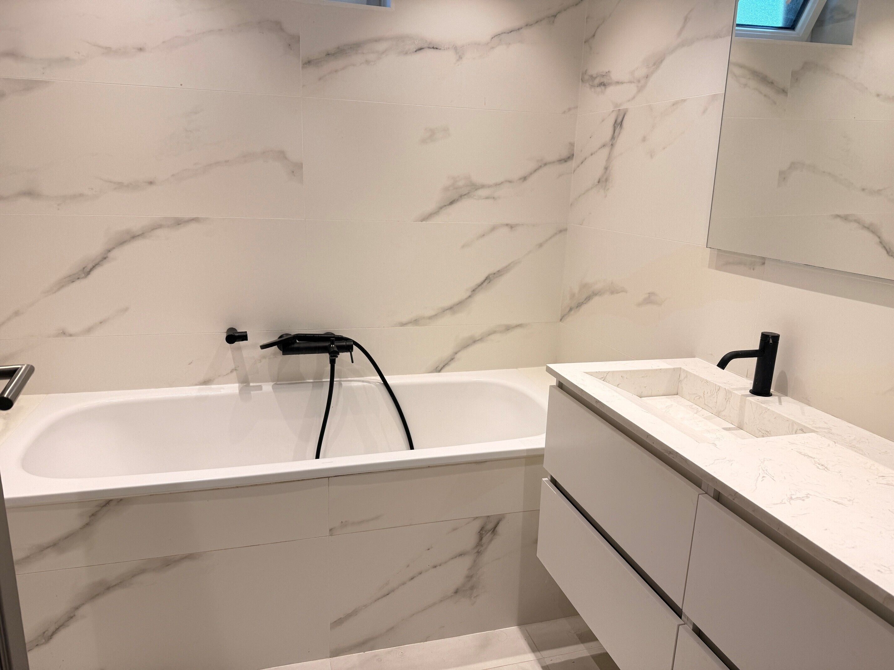 Une salle de bain avec une baignoire en marbre blanc, un robinet noir et un plan de toilette en marbre blanc avec un lavabo noir.